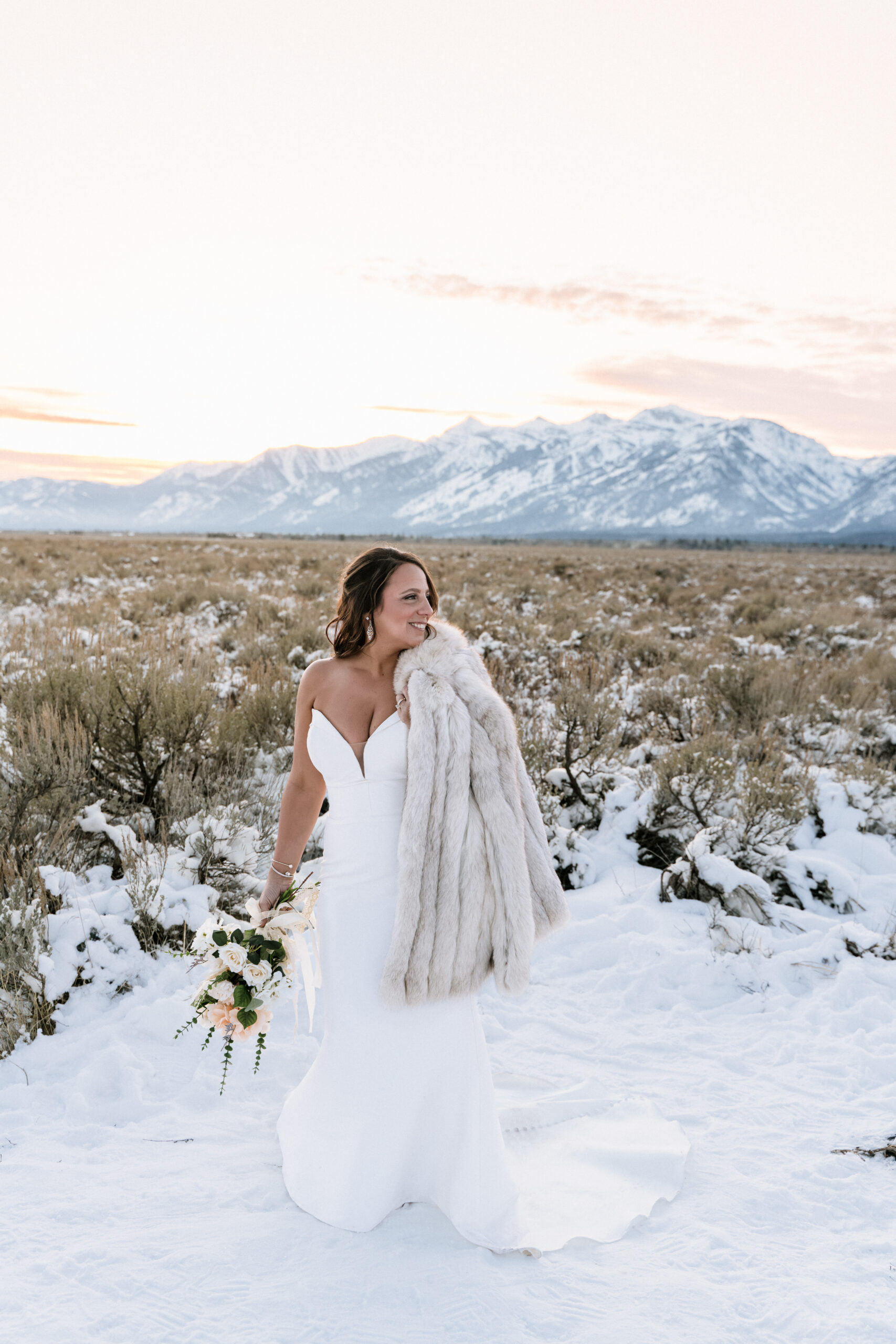 Bride in a white wedding dress standing in the snow at Snake River Overlook in Grand Teton National Park during a winter elopement